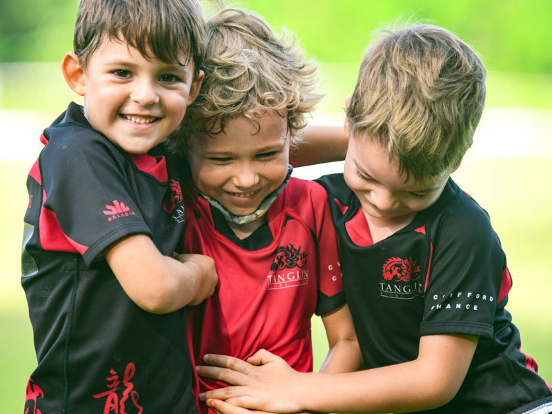 three young boys hugging smiling outdoors rugby for kids sports club