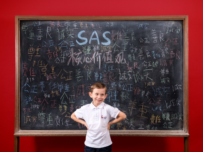 SingaporeAmericanSchool male student in front of blackboard with Chinese words Mandarin language programme
