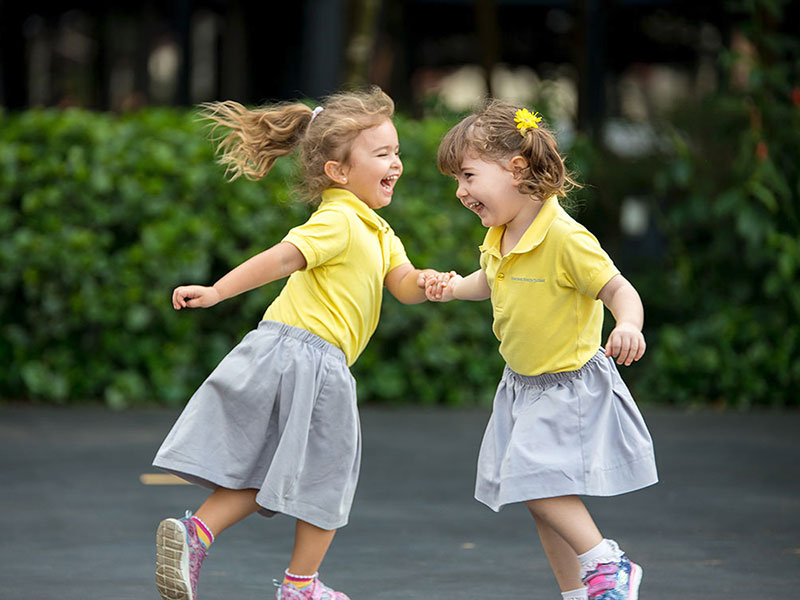 Overseas Family School international school preschool curriculum two girls laughing & playing outdoors