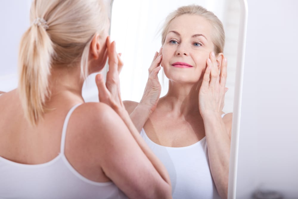 older ageing woman looking in mirror and pulling back face