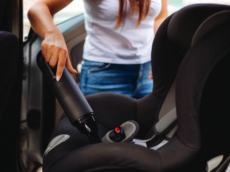 lady cleaning baby car seat with hand vacuum