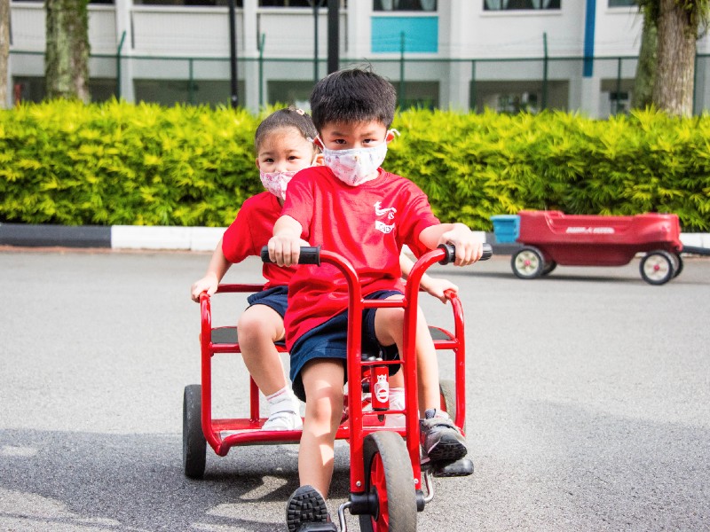 Singapore American School two pre-kindergarten kids on tricycle outdoors